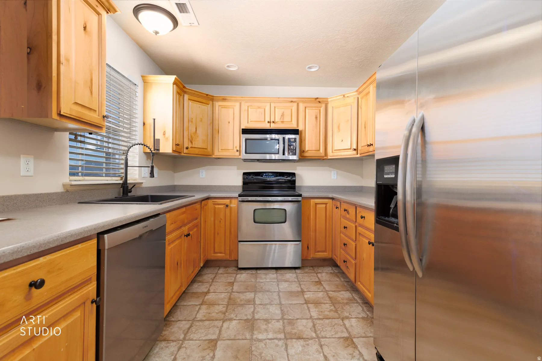 U-shaped kitchen featuring light wood cabinetry, stone-finish countertops, and stainless steel appliances including a refrigerator, range, microwave, and dishwasher