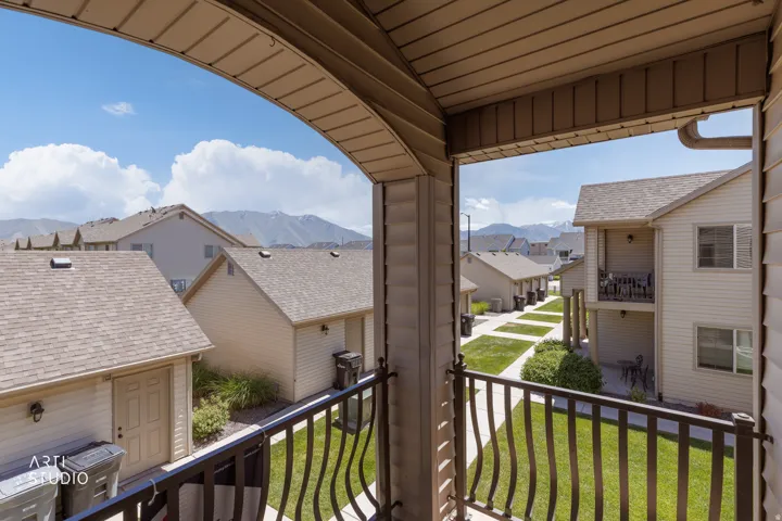 Covered balcony with decorative metal railing overlooking a community courtyard with manicured lawns and mountain scenery