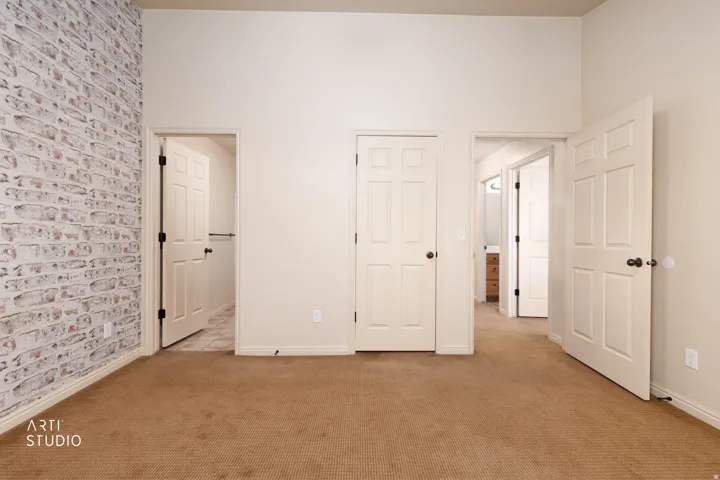 Interior space featuring textured brick-patterned wall, neutral carpeting, and multiple panel doors