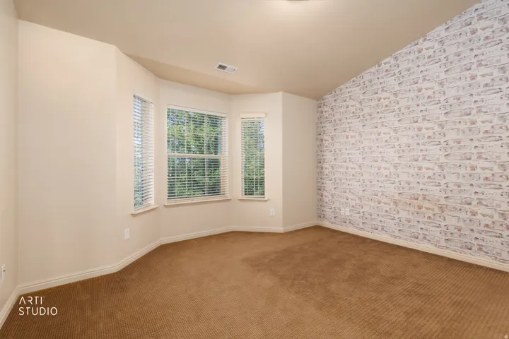 Room featuring a multi-paned bay window with blinds, a prominent accent wall with a distressed brick finish, and neutral-toned carpeting