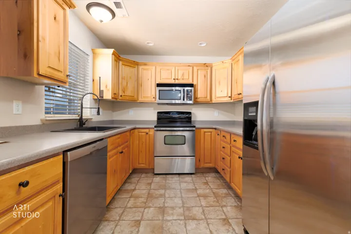 U-shaped kitchen featuring light wood cabinetry, stone-finish countertops, and stainless steel appliances including a refrigerator, range, microwave, and dishwasher