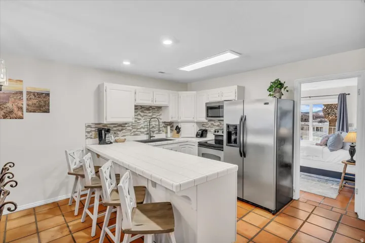 Kitchen featuring white cabinetry, tile countertops, stainless steel appliances, a patterned tile backsplash, and terracotta-style floor tiles