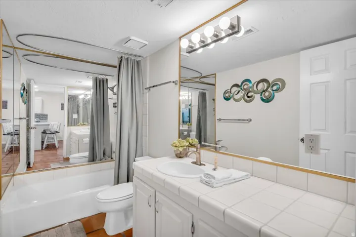 Bathroom featuring a full vanity with an integrated sink, white tiled countertop, and a large mirror with a brass-finish frame