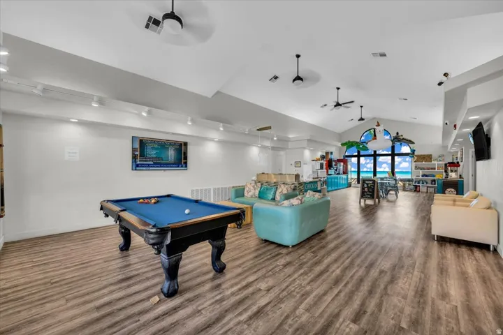 Spacious entertainment room featuring wood-finish flooring and a vaulted ceiling with multiple ceiling fans