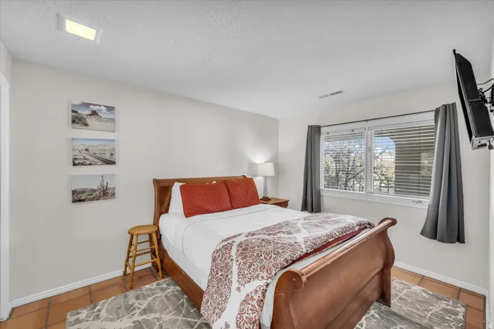 Bedroom featuring terra cotta tile flooring, a window with horizontal blinds, and a ceiling-mounted light fixture