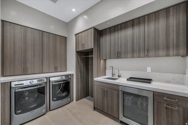 Utility room featuring extensive wood-finish cabinetry, light-toned countertops, a built-in sink with a gooseneck faucet, and a stainless steel under-counter refrigerator