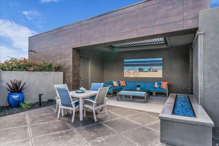 Spacious rooftop patio featuring large format tile flooring, a built-in fire pit with blue glass rocks, a covered lounge area, and raised planters