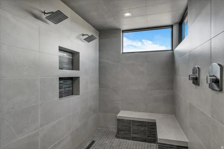 Spacious shower with two rainfall showerheads, a built-in bench, recessed display niches with mosaic tile accents, and a transom window