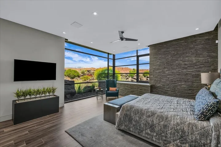 Expansive floor-to-ceiling windows with black framing, wood-finish flooring, a contemporary ceiling fan, recessed lighting, and a textured stone accent wall
