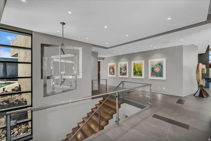 Contemporary staircase featuring wood-finish treads, glass railings with metal handrails, and a modern chandelier