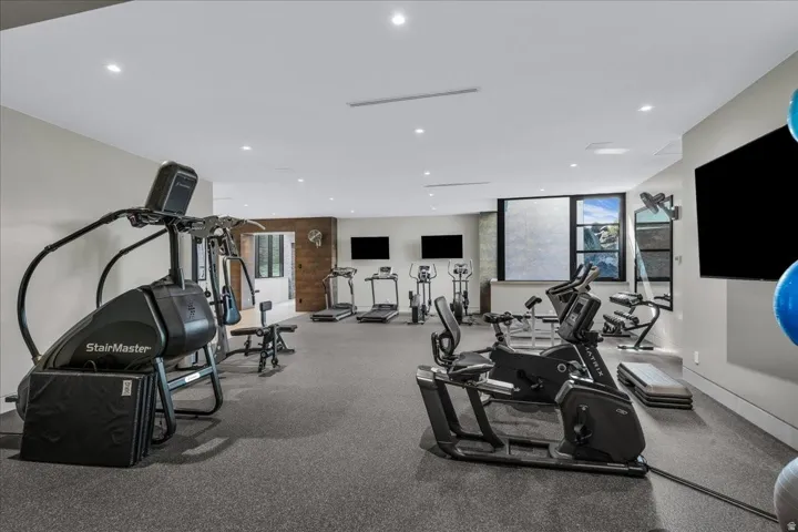 Dedicated fitness room featuring recessed lighting, durable rubber flooring, multiple flat-screen televisions, and large windows