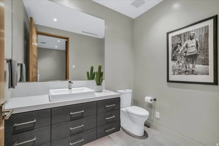 Modern powder room featuring a rectangular vessel sink, a light-toned countertop, a dark wood-finish vanity with ample storage, a large wall-mounted mirror, and tile flooring