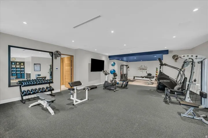 Spacious home gym featuring rubber flooring, recessed lighting, a large wall-mounted mirror, and an accent wall with a blue bulkhead