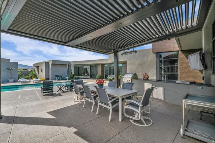 Covered outdoor living area featuring a louvered patio cover, built-in outdoor kitchen with grill, pool, and concrete patio