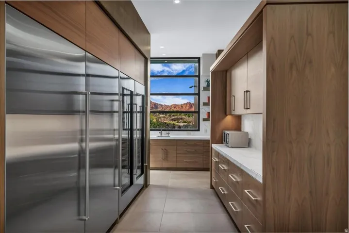 Contemporary kitchen featuring integrated stainless steel appliances, custom wood cabinetry, a built-in beverage refrigerator, and a window with mountain scenery