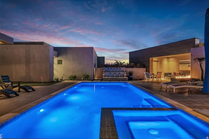 Illuminated swimming pool with integrated spa, surrounded by a paved patio