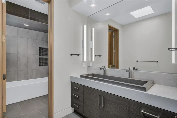Contemporary bathroom featuring a dark wood-finish vanity with a light countertop, integrated rectangular sink, and dual wall-mounted faucets
