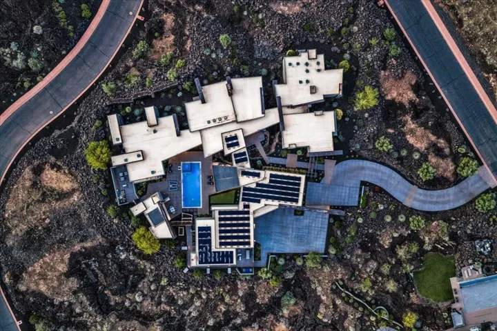 Architectural compound featuring multiple flat-roof structures, a central swimming pool, extensive solar panel arrays, and a winding paved pathway