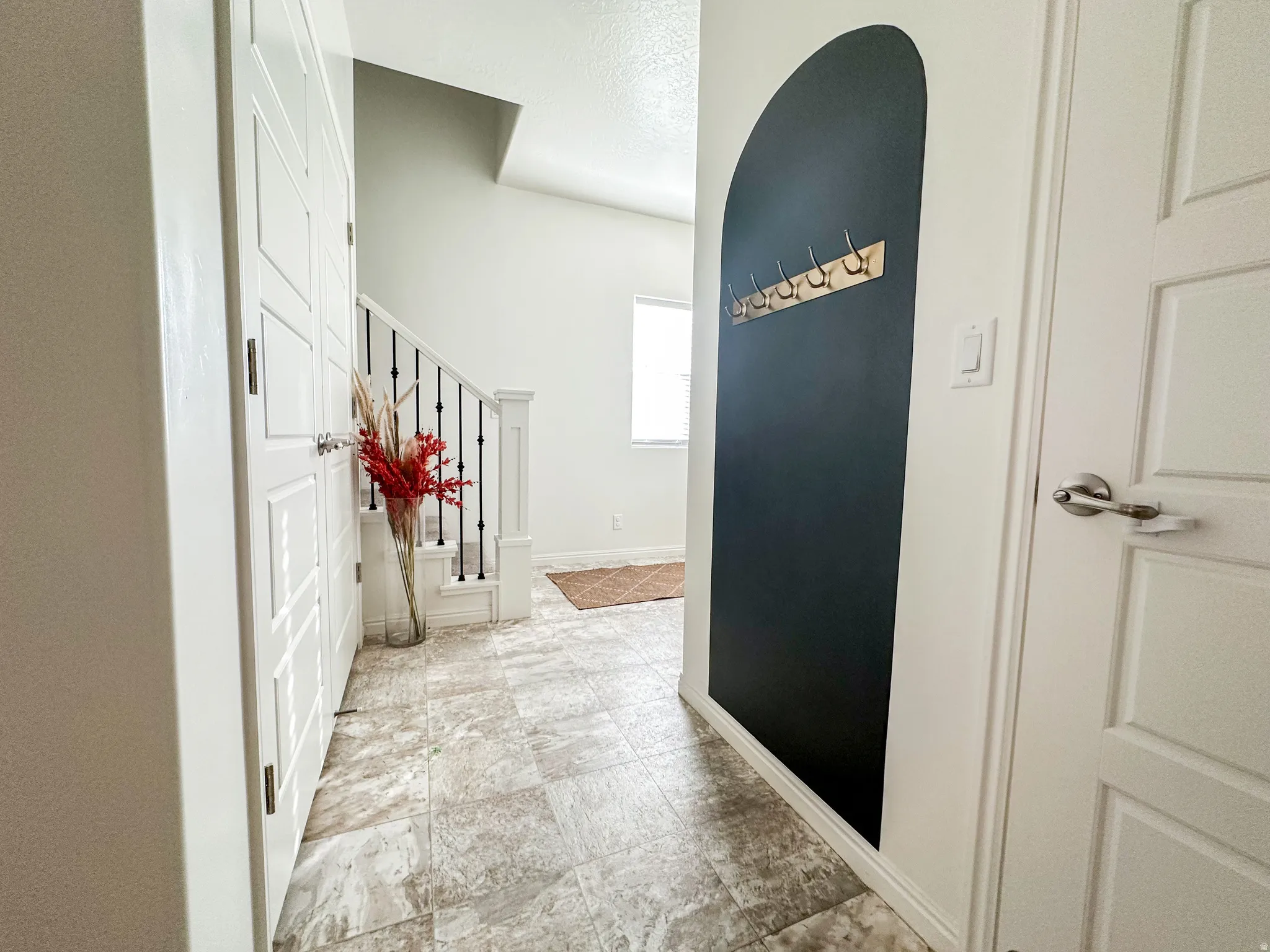 Tiled entryway with paneled doors, a built-in coat rack, and a staircase featuring black metal balusters