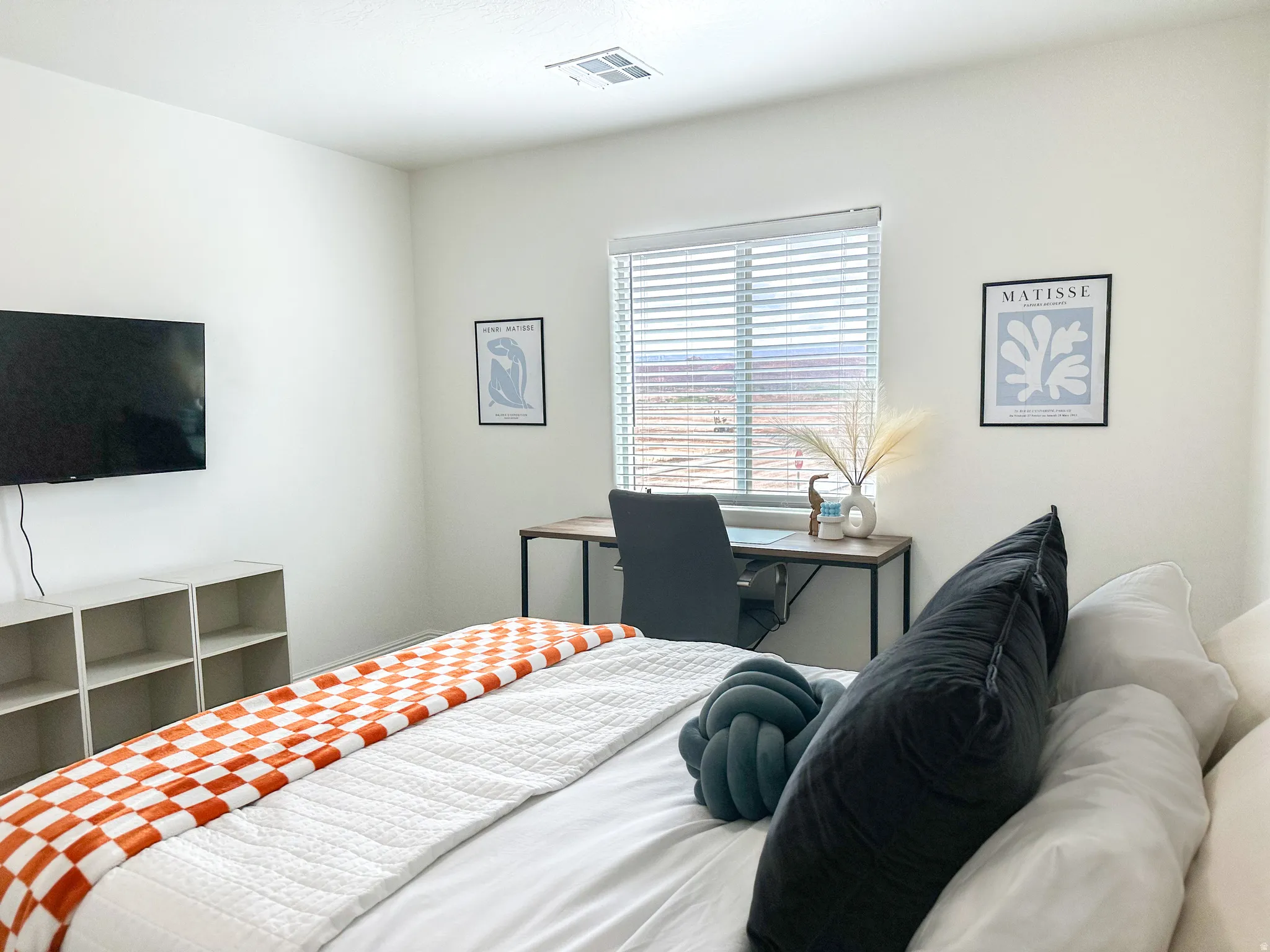 Bedroom featuring a large window with horizontal blinds, a wall-mounted television, and light-toned walls