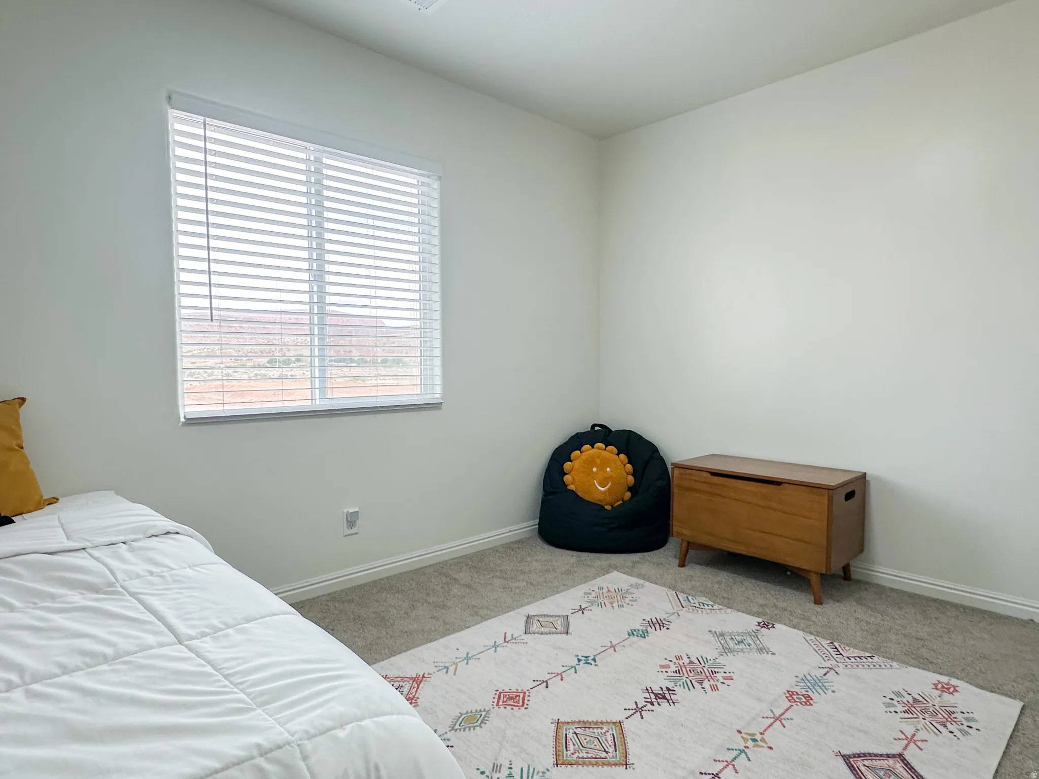 Bedroom with neutral wall paint and carpeting, featuring a window with horizontal blinds and a baseboard