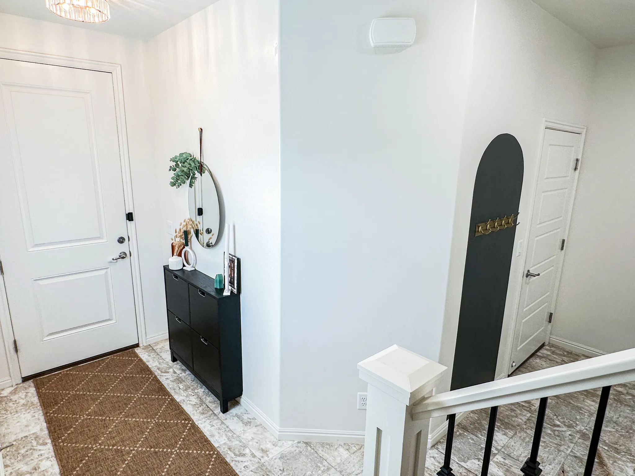 Entryway featuring a decorative ceiling light fixture, a paneled door with brushed nickel hardware, light-toned tile flooring, and a staircase with white newel posts and black wrought iron balusters