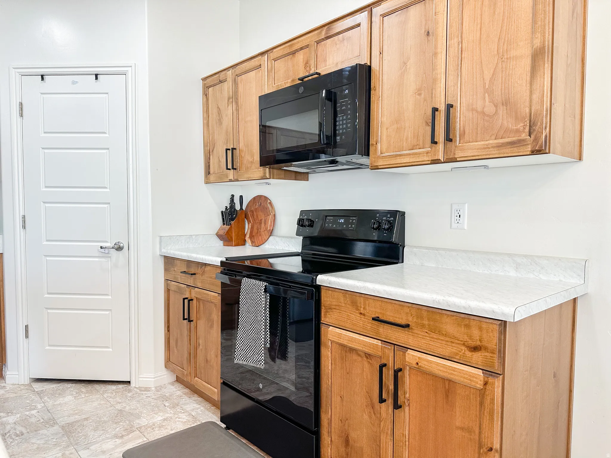 Kitchen featuring natural wood cabinetry, white countertops, a black electric range, and a built-in microwave