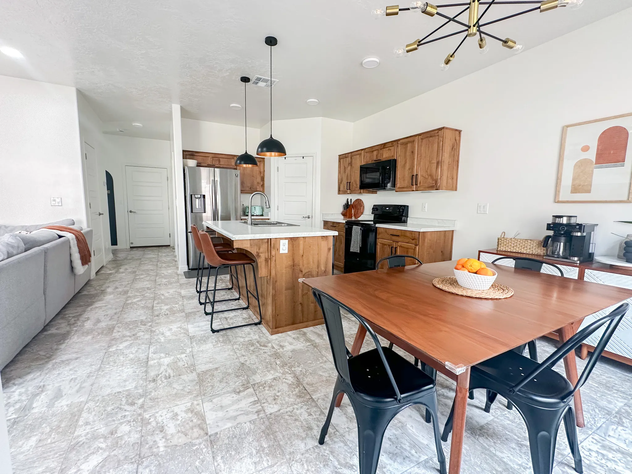 Open-concept living area featuring a kitchen island with pendant lighting, wood-finish cabinetry, light-toned countertops, and stainless steel appliances