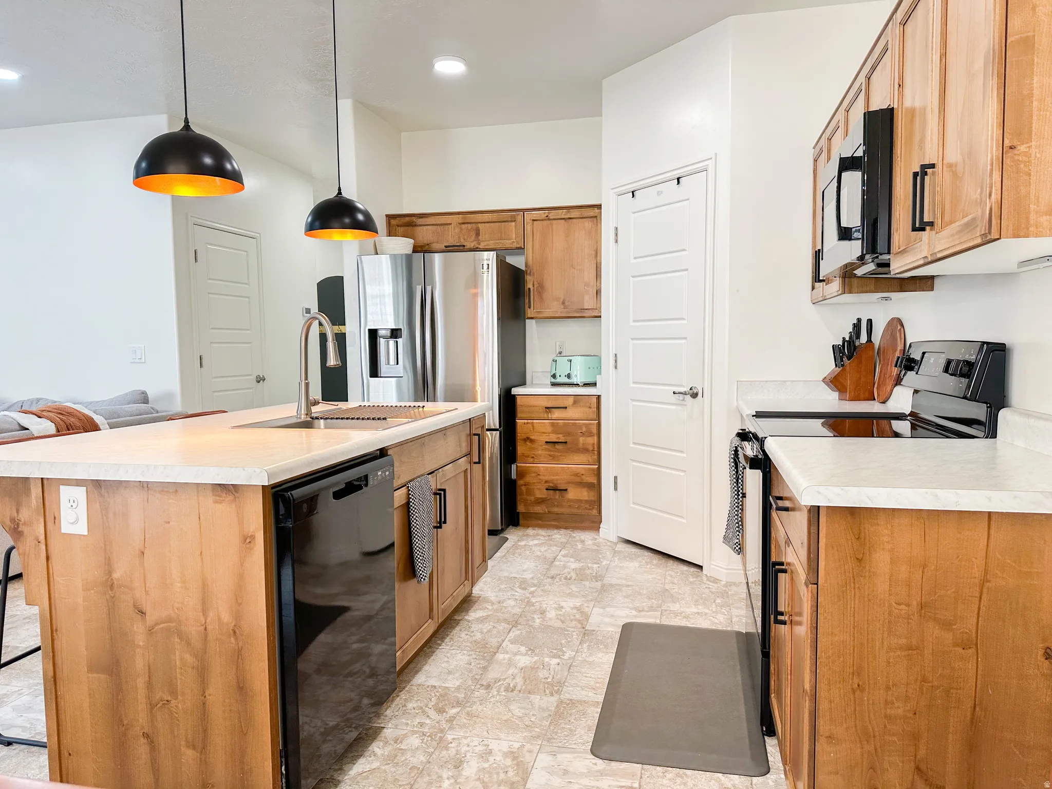 Kitchen featuring a center island with sink and dishwasher, wood-finish cabinetry, stainless steel refrigerator, and integrated cooktop with microwave