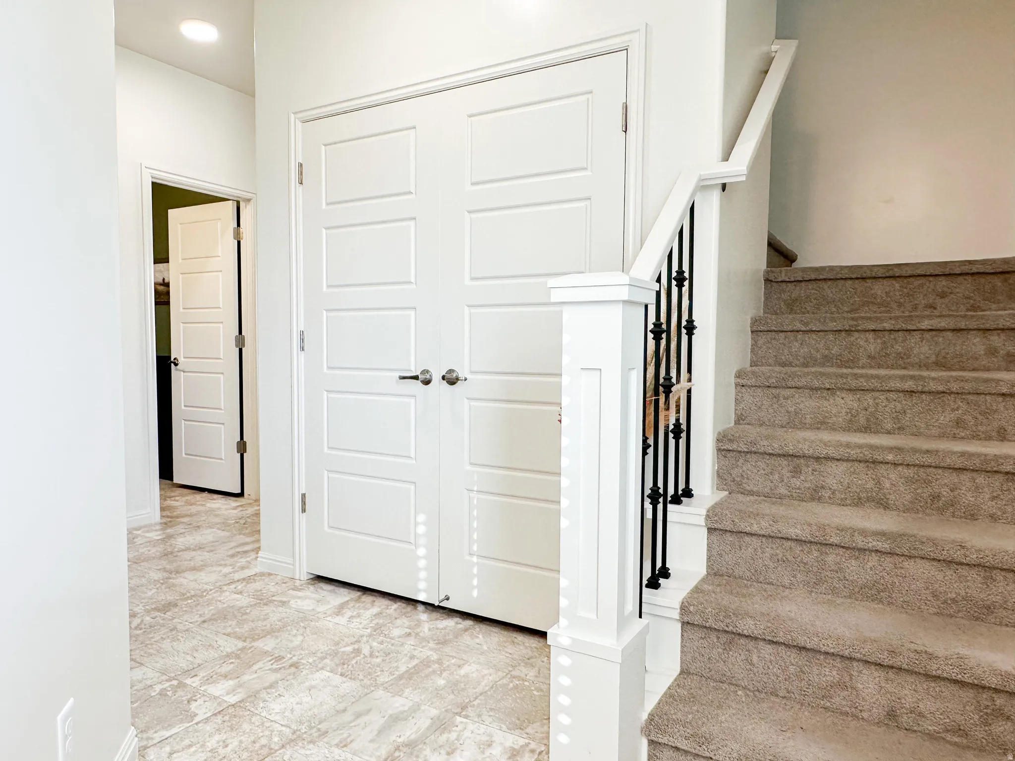 Foyer featuring large format floor tiling, white paneled doors, recessed lighting, and a staircase with a white newel post and black iron balusters