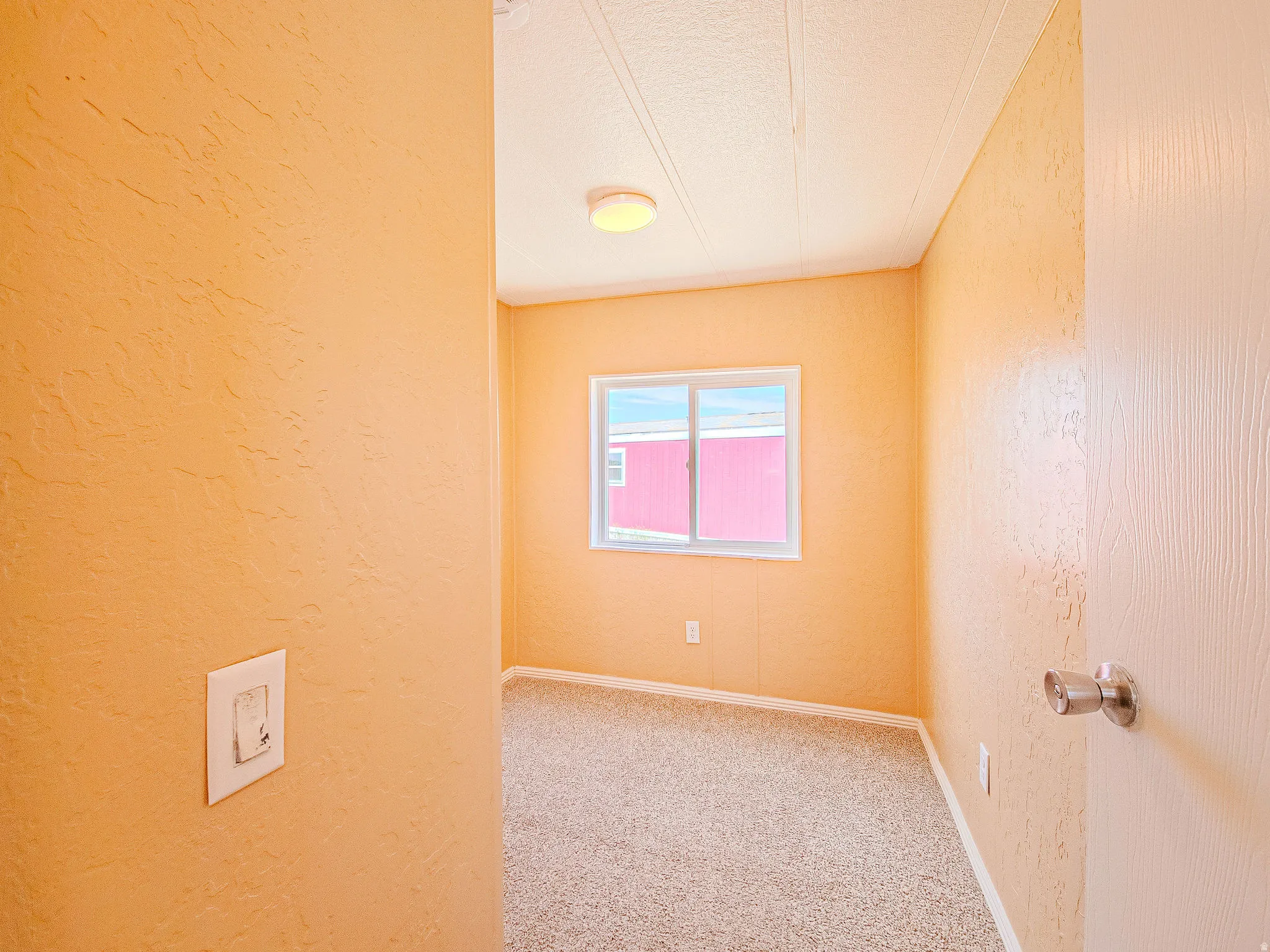 Room featuring textured orange walls, a white framed window, and light-colored carpet flooring