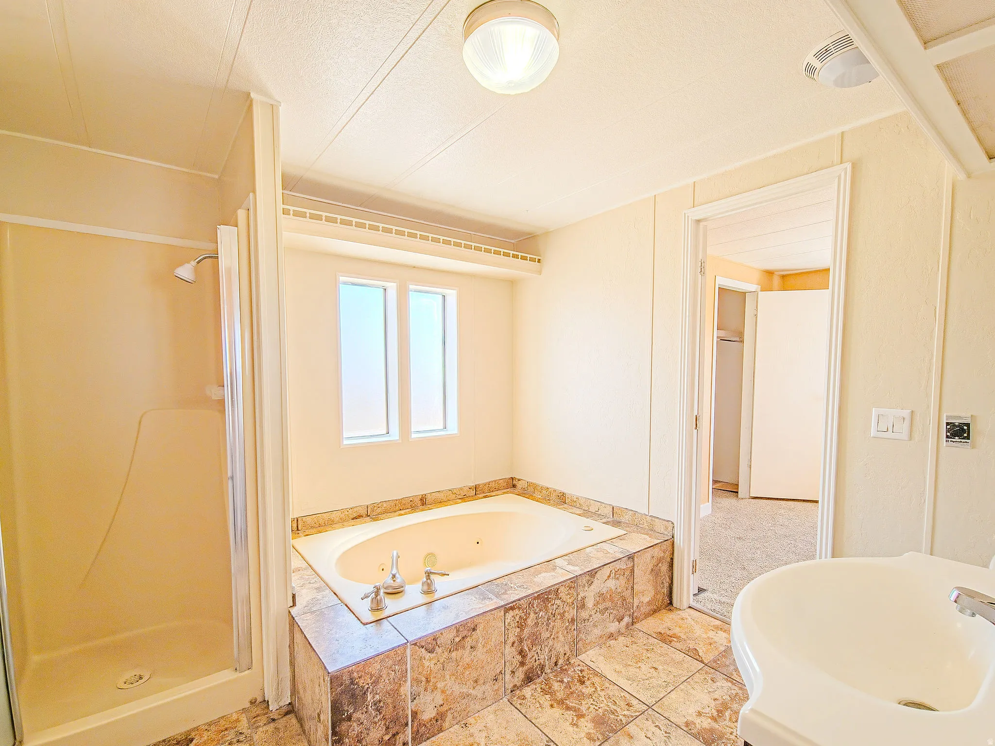 Bathroom featuring a built-in jetted tub with a tiled surround, a separate shower enclosure, and a vanity with a basin sink