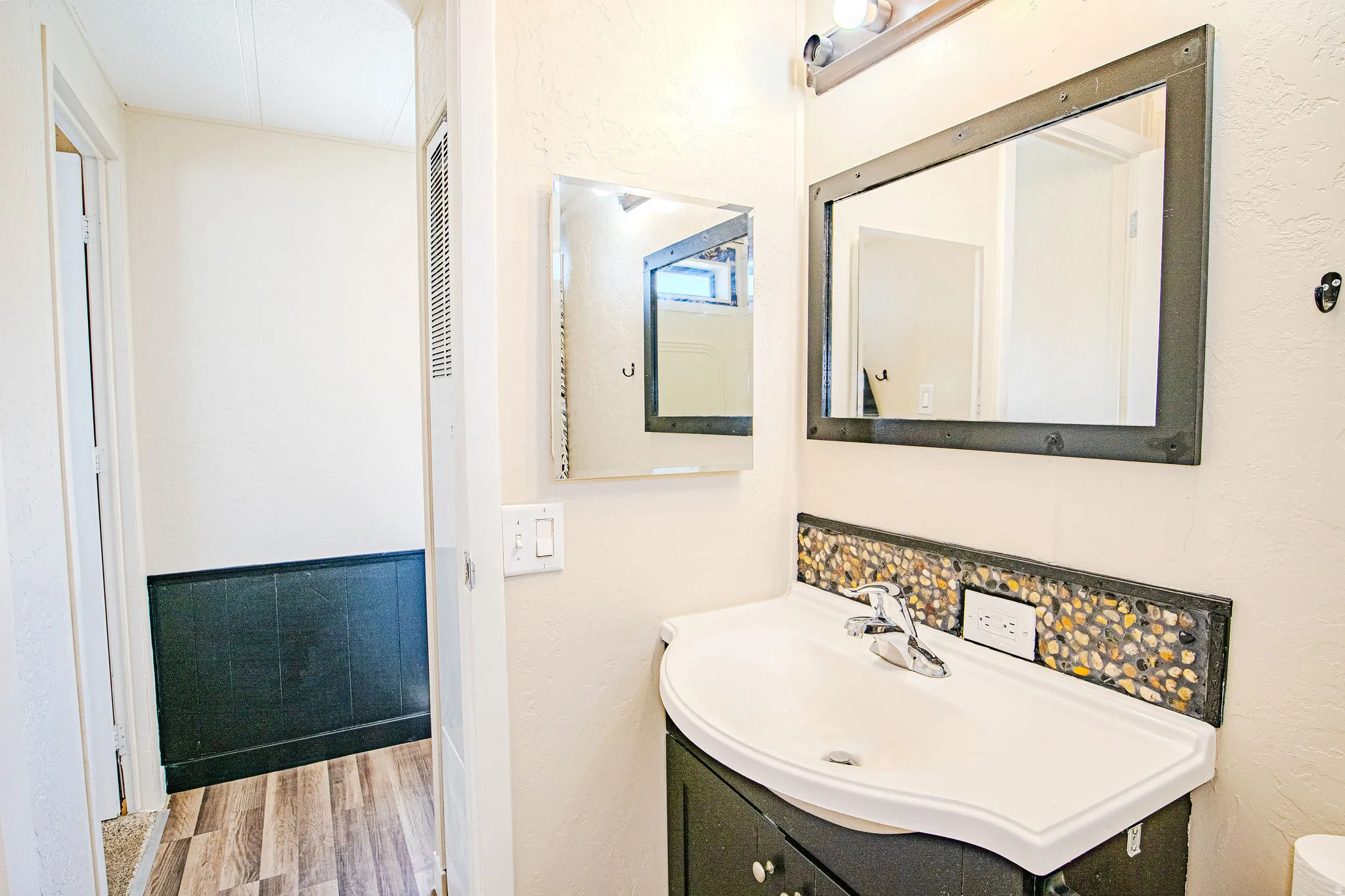 Vanity with integrated sink, pebble tile backsplash, and dark wood-finish cabinetry