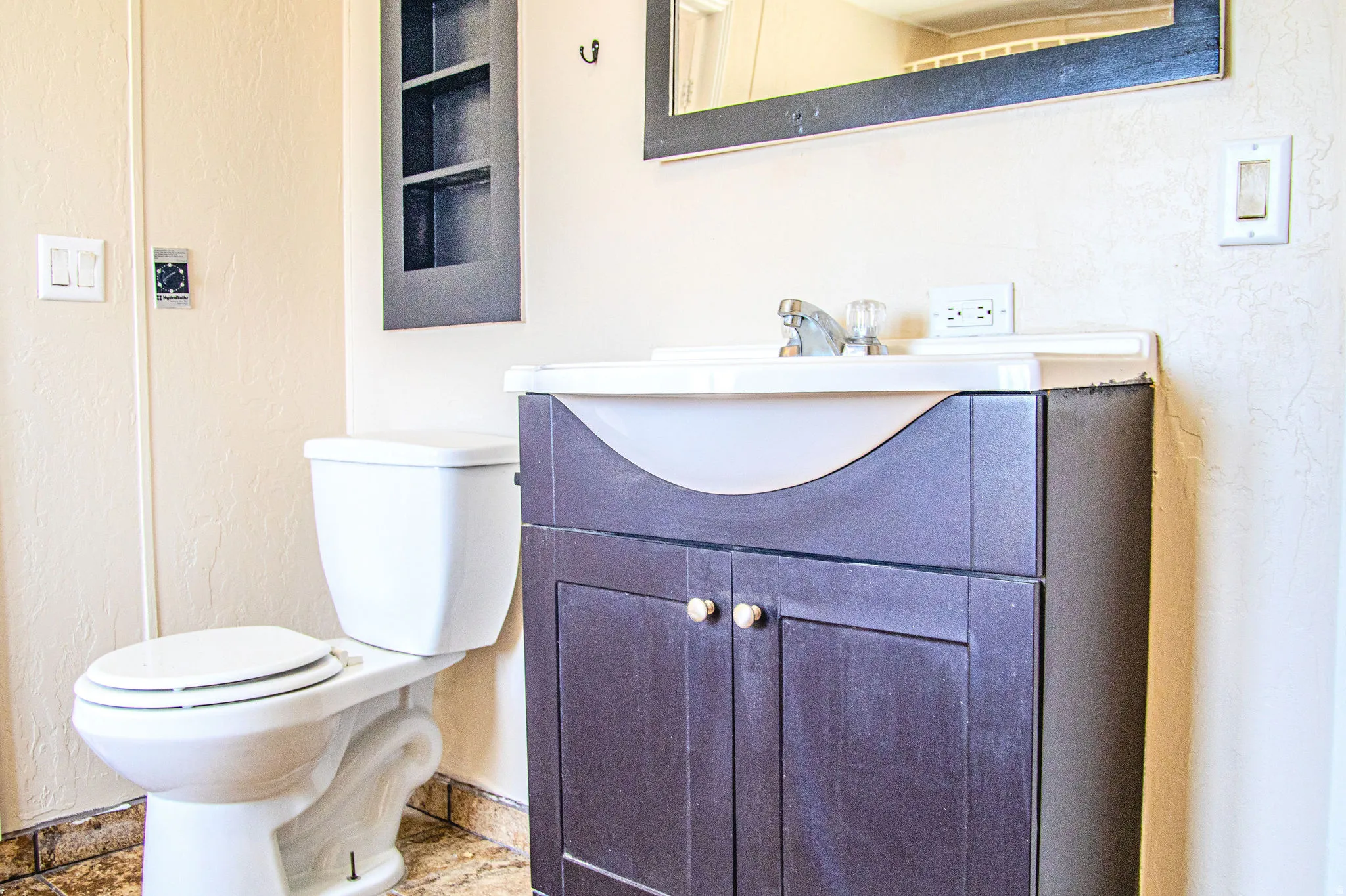Bathroom featuring a dark wood-finish vanity with an integrated white sink, a mirror with a dark frame, and a white toilet