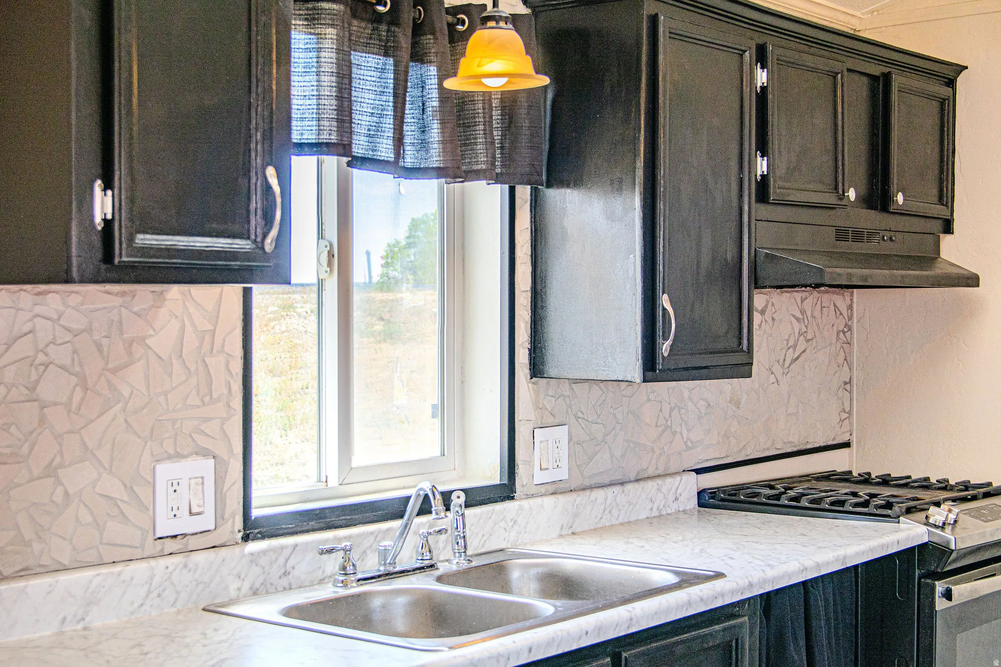 Kitchen featuring black cabinetry, light-toned countertops, a double basin stainless steel sink, and a gas range