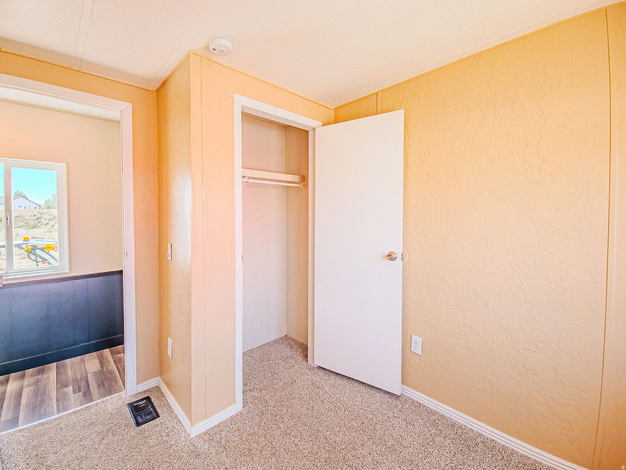 Carpeted room featuring a white door, a built-in closet with a hanging rod, and textured walls