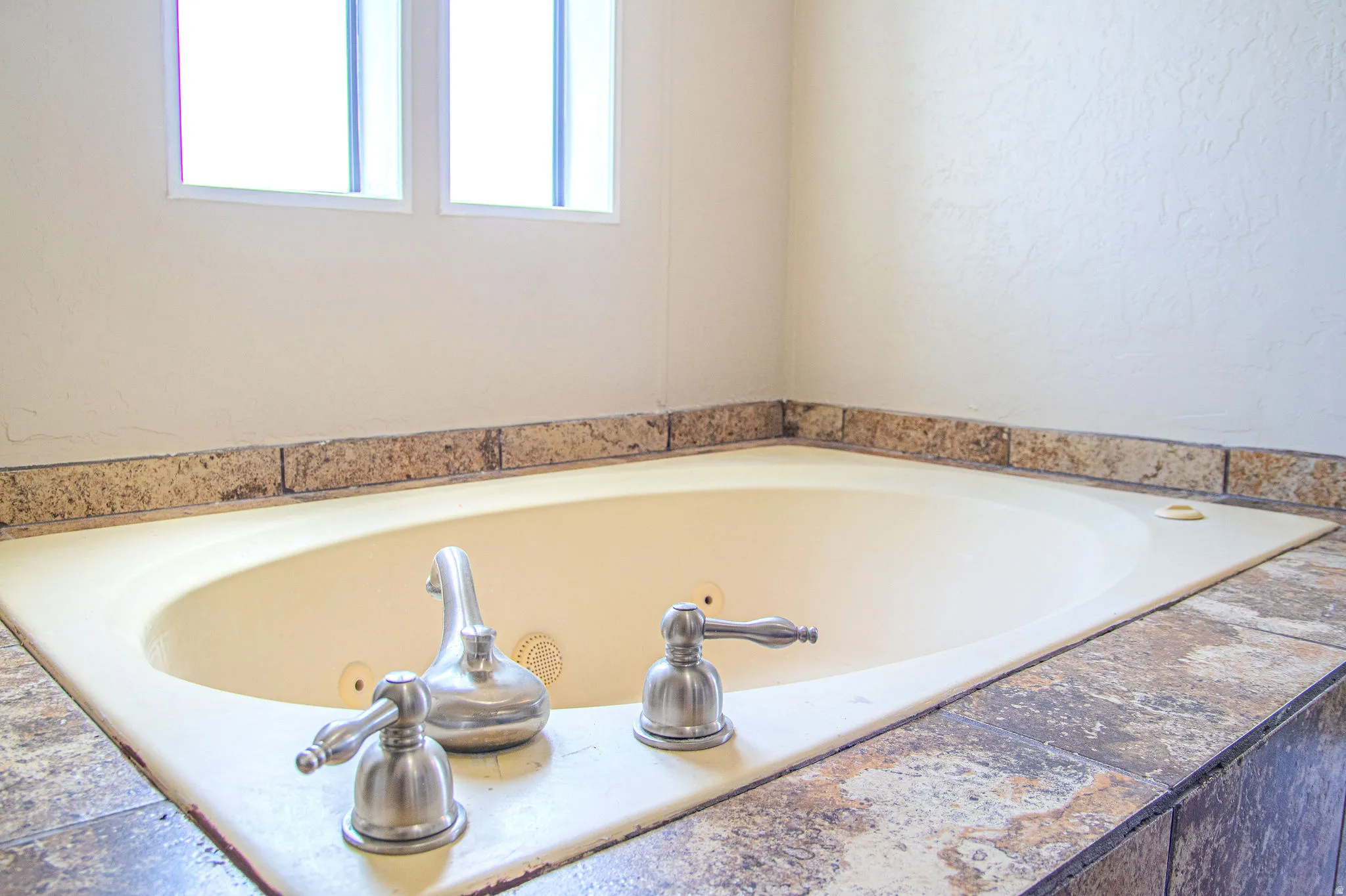 Built-in soaking tub with brushed nickel fixtures and a tiled surround