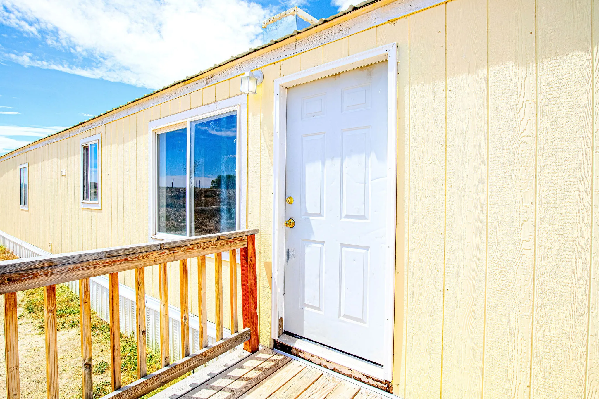 Yellow exterior siding featuring a white paneled entry door, white trim windows, and an exterior wall light fixture