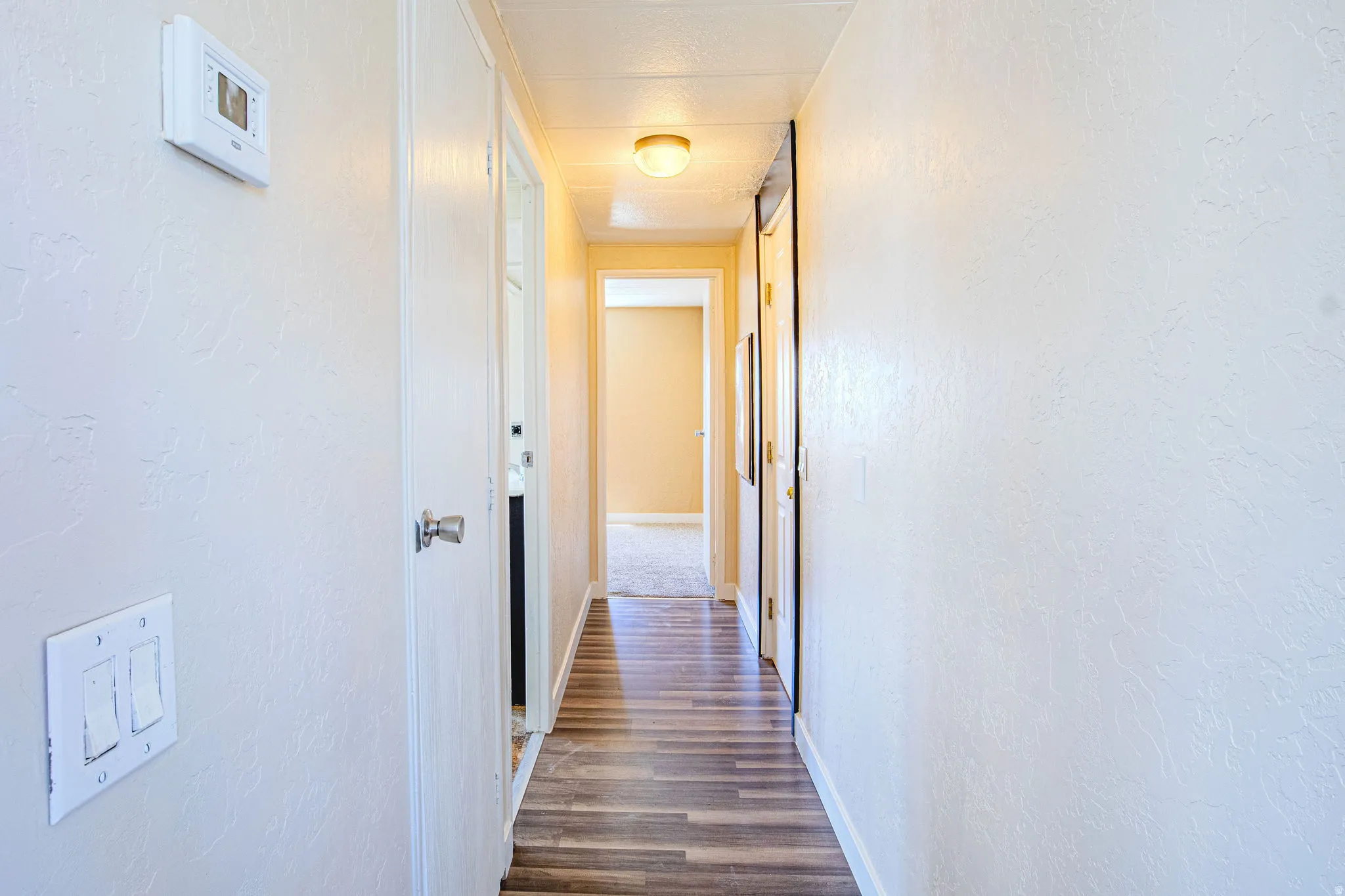Hallway with wood-finish flooring, light-toned walls, and multiple white doors