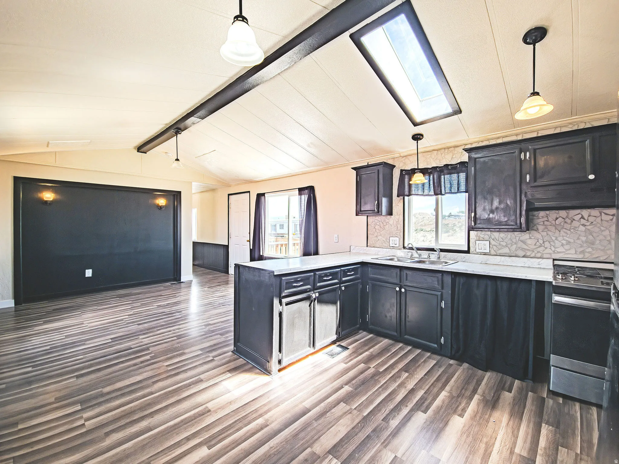 Open concept living area featuring wood-finish flooring, a vaulted ceiling, and a skylight