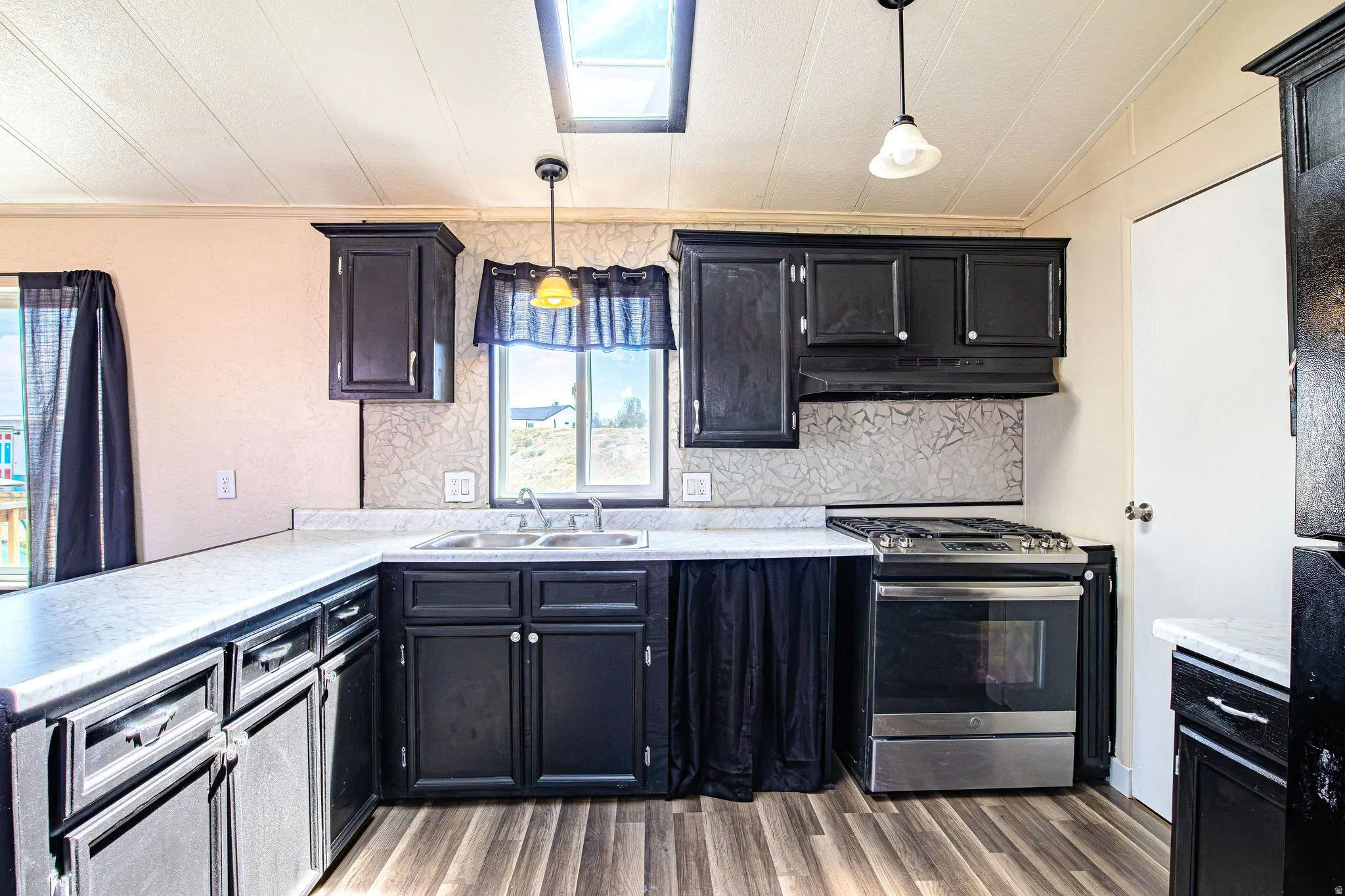 Kitchen featuring dark cabinetry, light countertops, wood-finish flooring, and a skylight