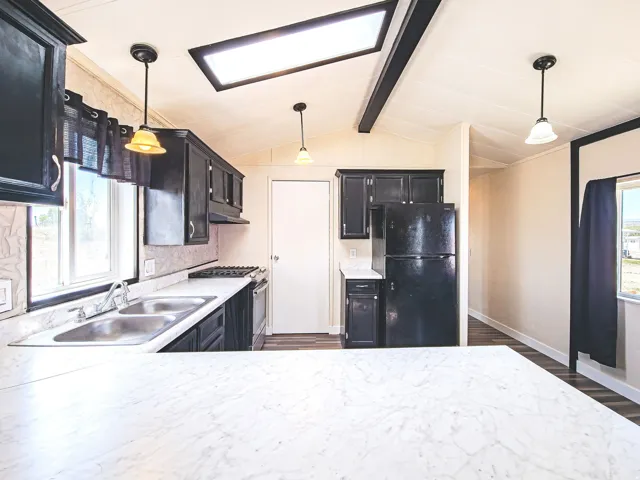 Kitchen featuring dark cabinetry, a double basin stainless steel sink, a gas range, and a full-size refrigerator