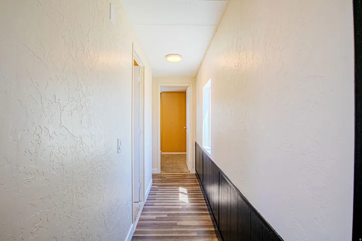 Hallway featuring wood-finish flooring, white textured walls, and dark paneling