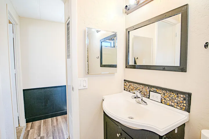 Vanity with integrated sink, pebble tile backsplash, and dark wood-finish cabinetry