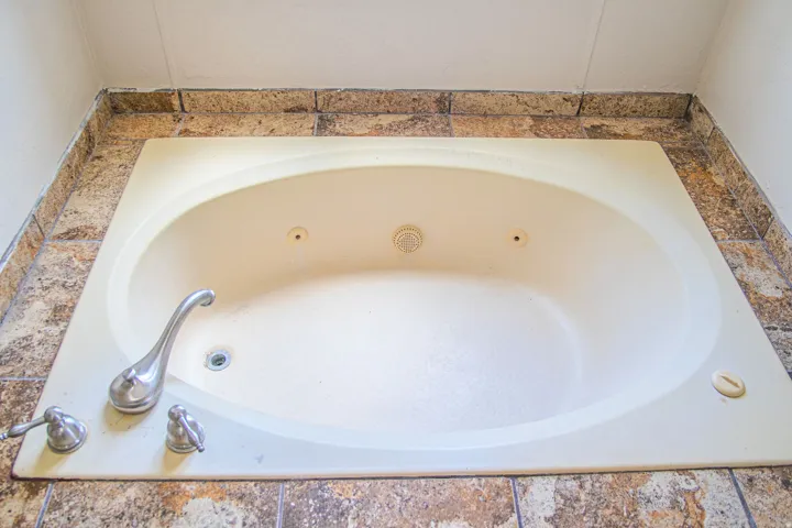 Built-in jetted tub with polished chrome fixtures, integrated drain, and stone-look tile surround
