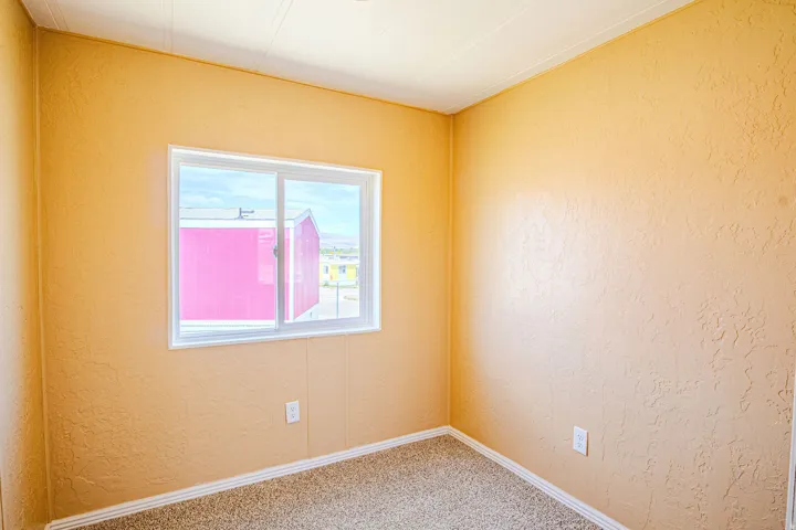 Room featuring a single white-framed window, textured wall finish, light-toned carpeting, white baseboards, and a white ceiling