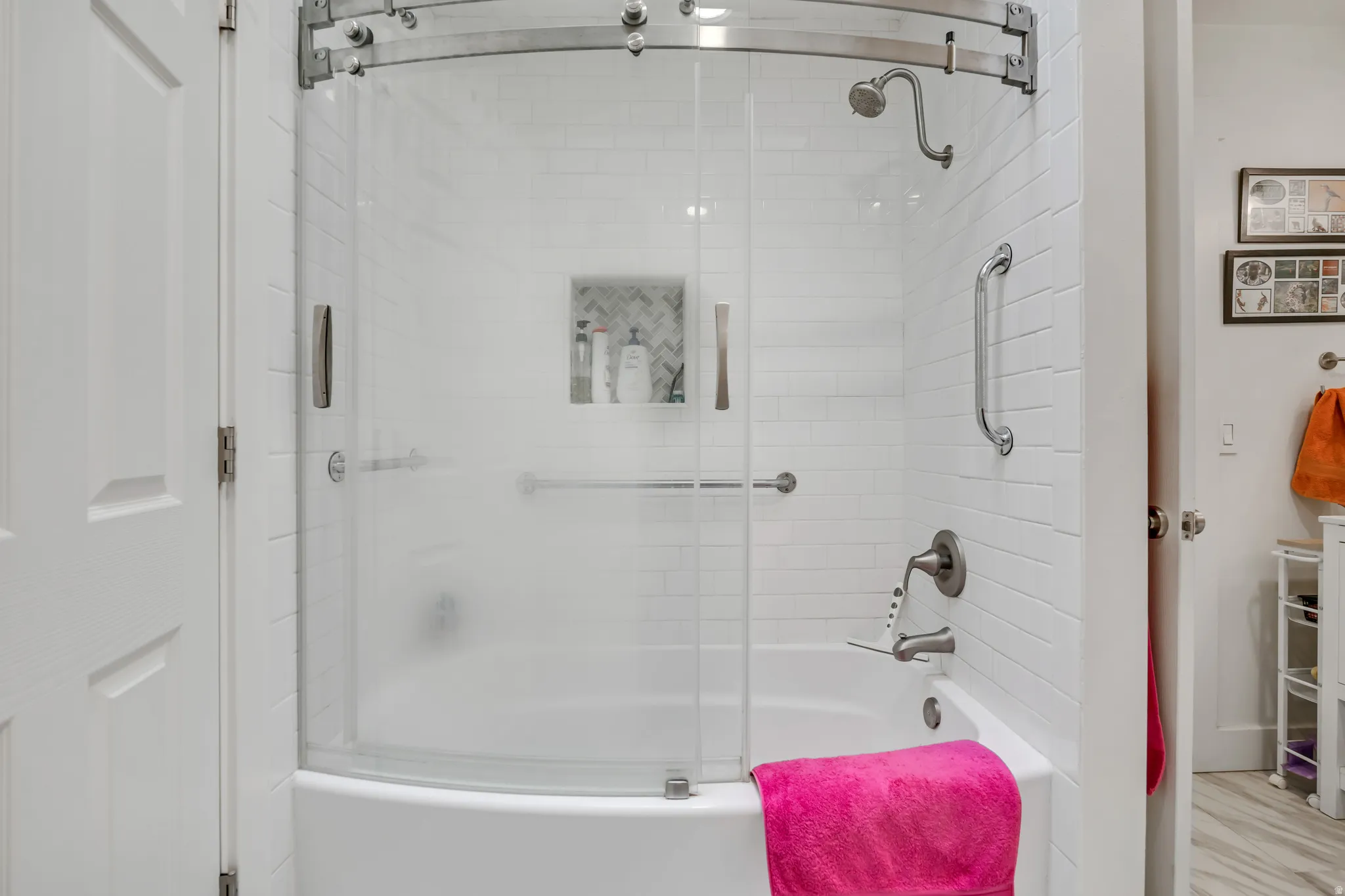 Tub and shower combination featuring white subway tile surround, a built-in shower niche with herringbone tile, brushed nickel fixtures, and curved glass sliding doors