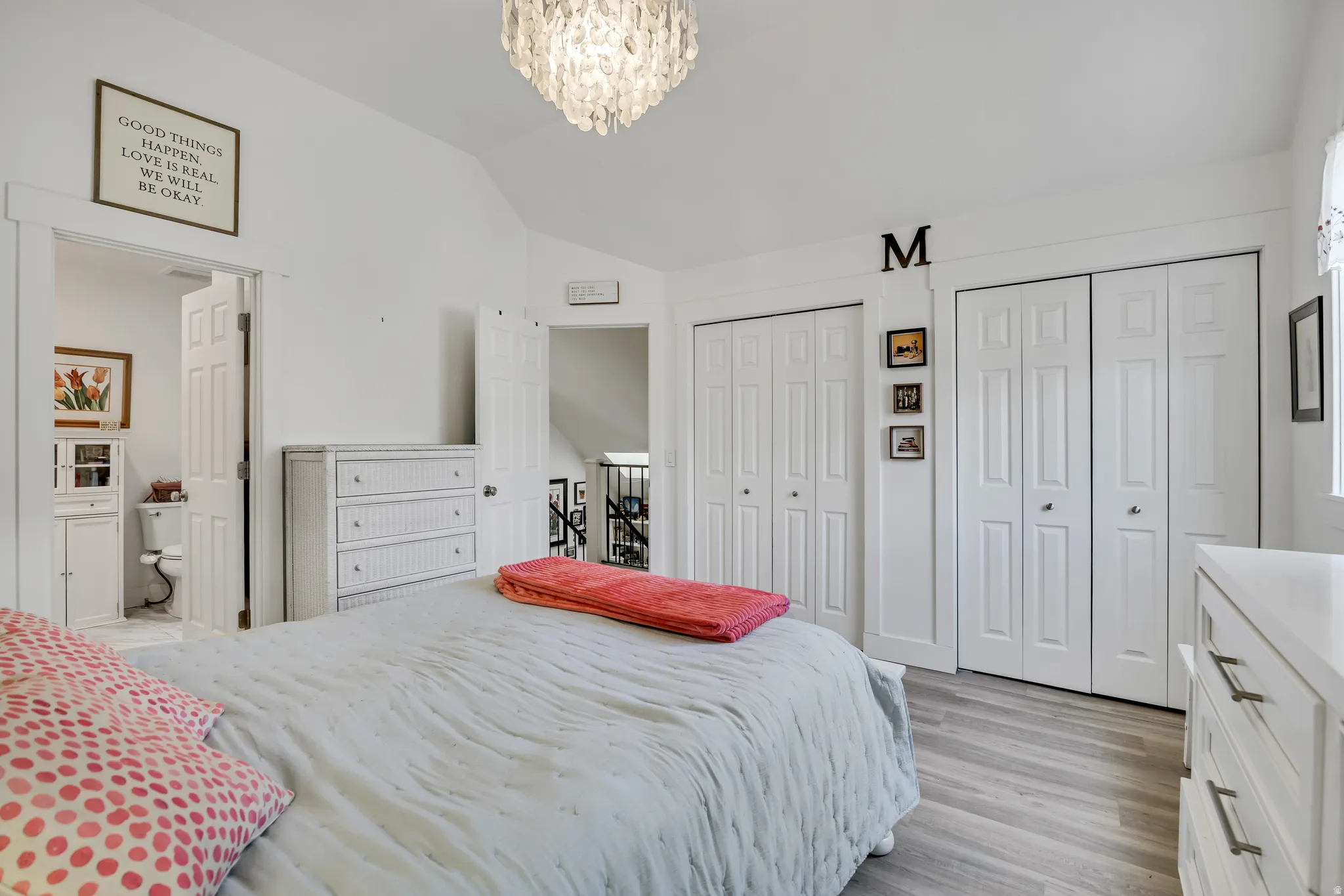 Vaulted ceiling bedroom featuring wood-finish flooring, a contemporary chandelier, and two sets of white bi-fold closet doors