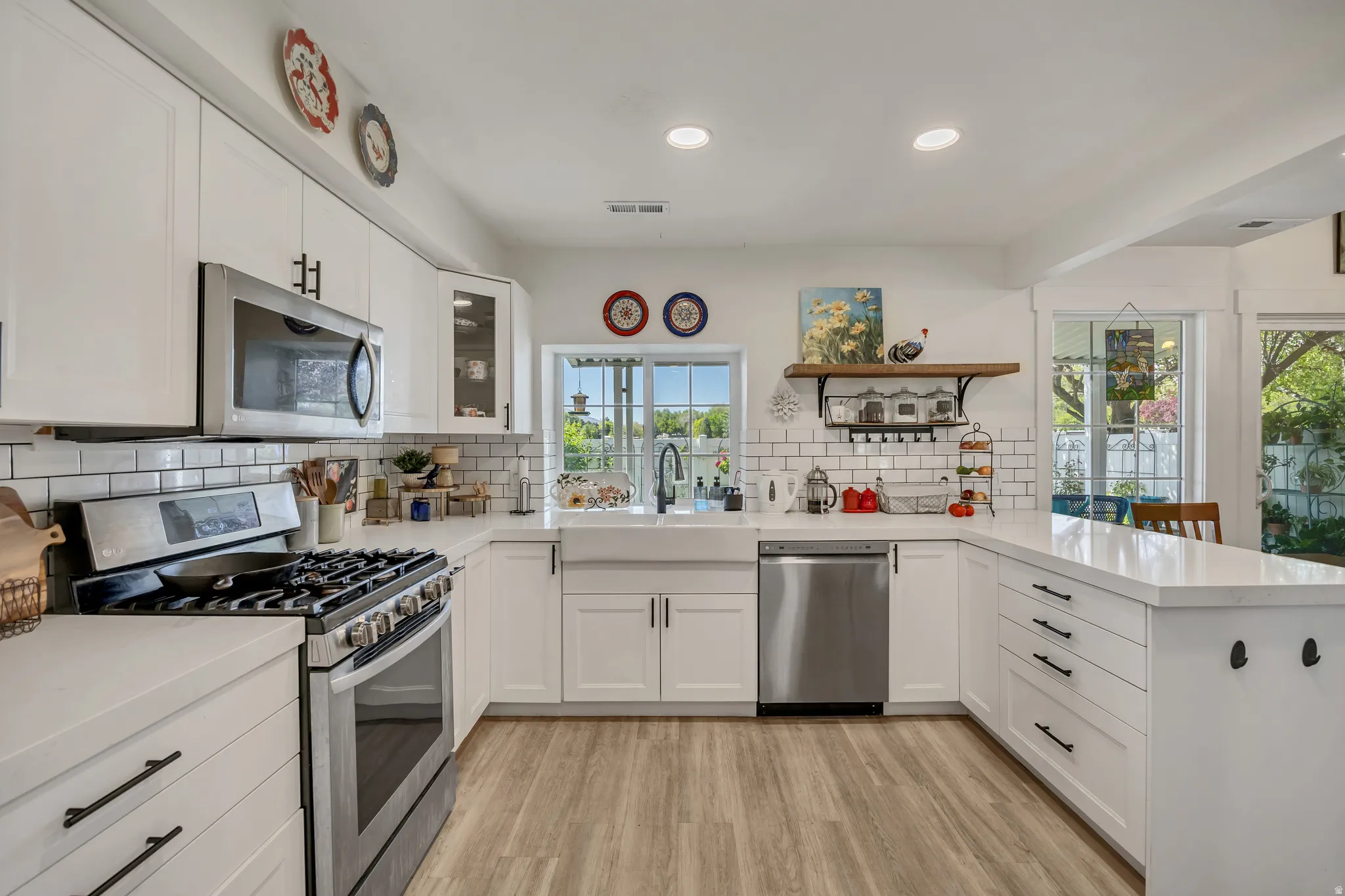 Modern kitchen featuring stainless steel appliances, white cabinetry with dark hardware, white subway tile backsplash, white countertops, and wood-finish flooring
