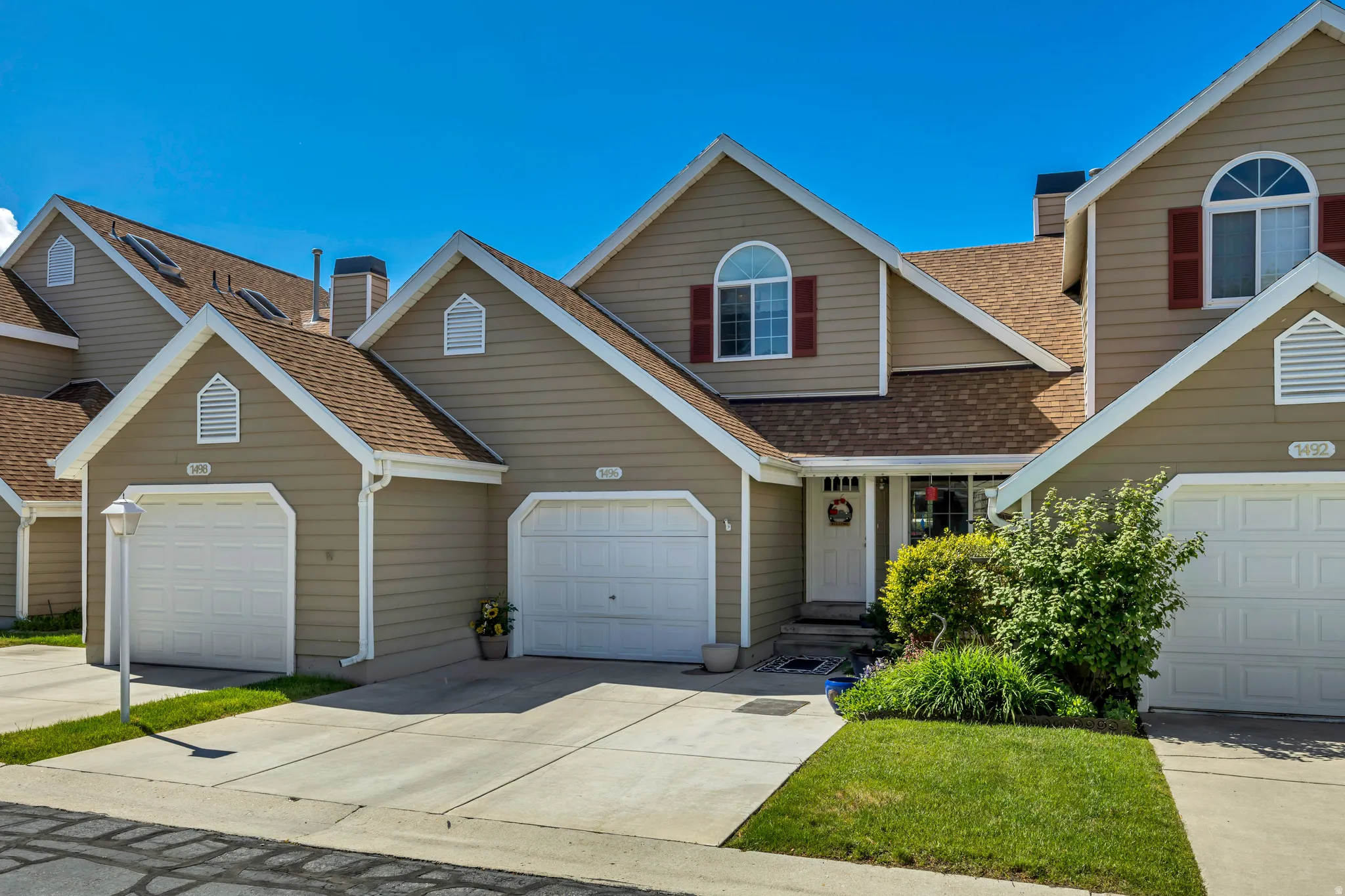 Exterior residence featuring tan siding, a combination of hip and gable roofs, and two attached garages with white doors